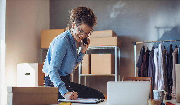 Caucasian Woman Sitting On Desk In Shop Taking Notes