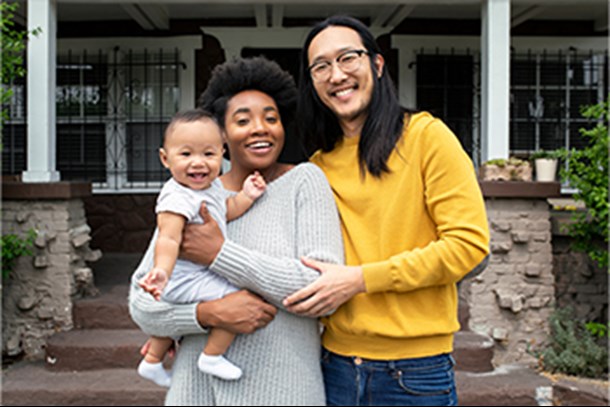 family of three in front of house